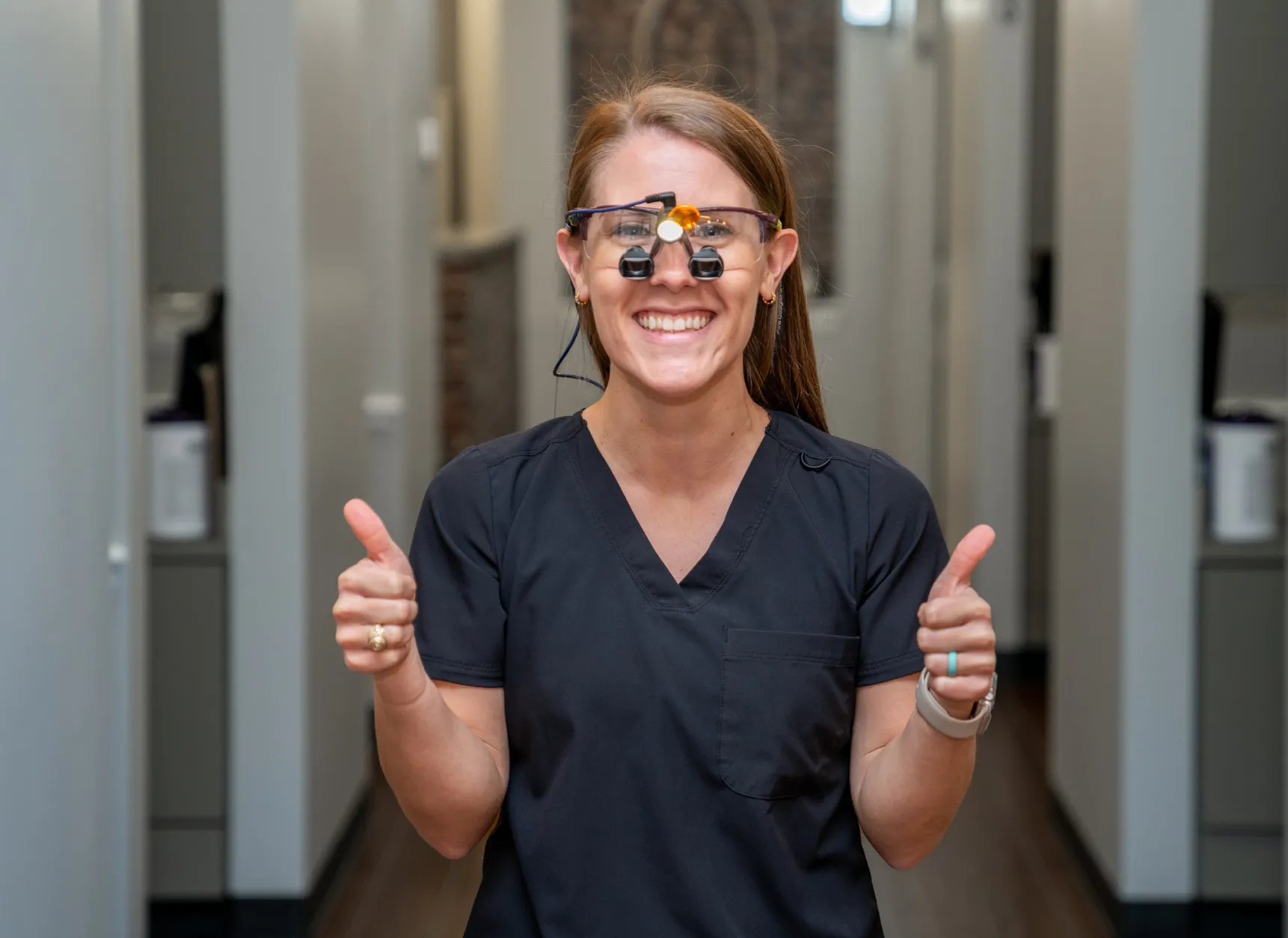 a woman in scrubs and glasses giving a thumbs up