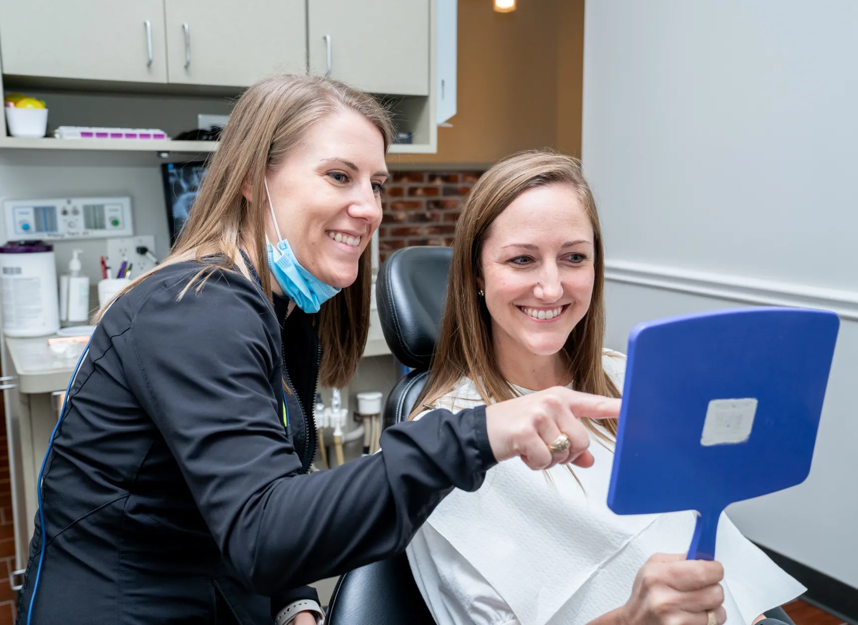 two women sitting in a dentist chair holding a blue toothbrush